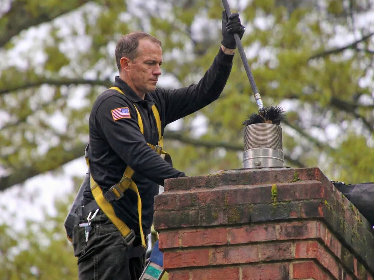 A Chimcare technician on a roof running a rotary brush down a chimney flue A Chimcare technician on a roof running a rotary brush down a chimney flue