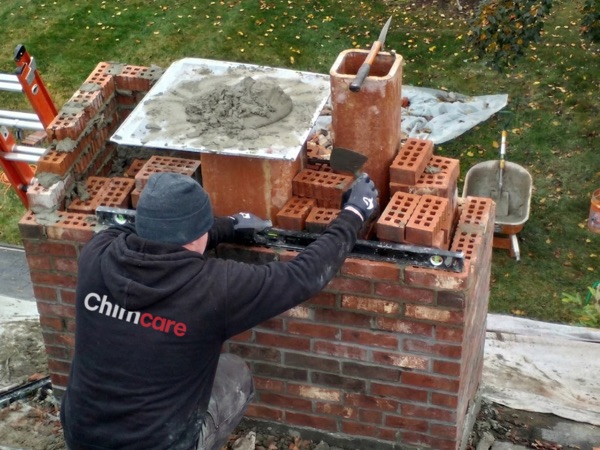 Mason repairing a masonry chimney on a rooftop