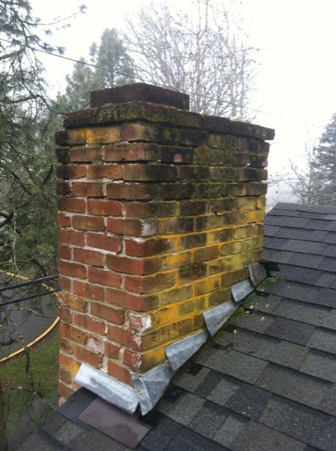 A brick chimney stained yellow and covered in moss before repair