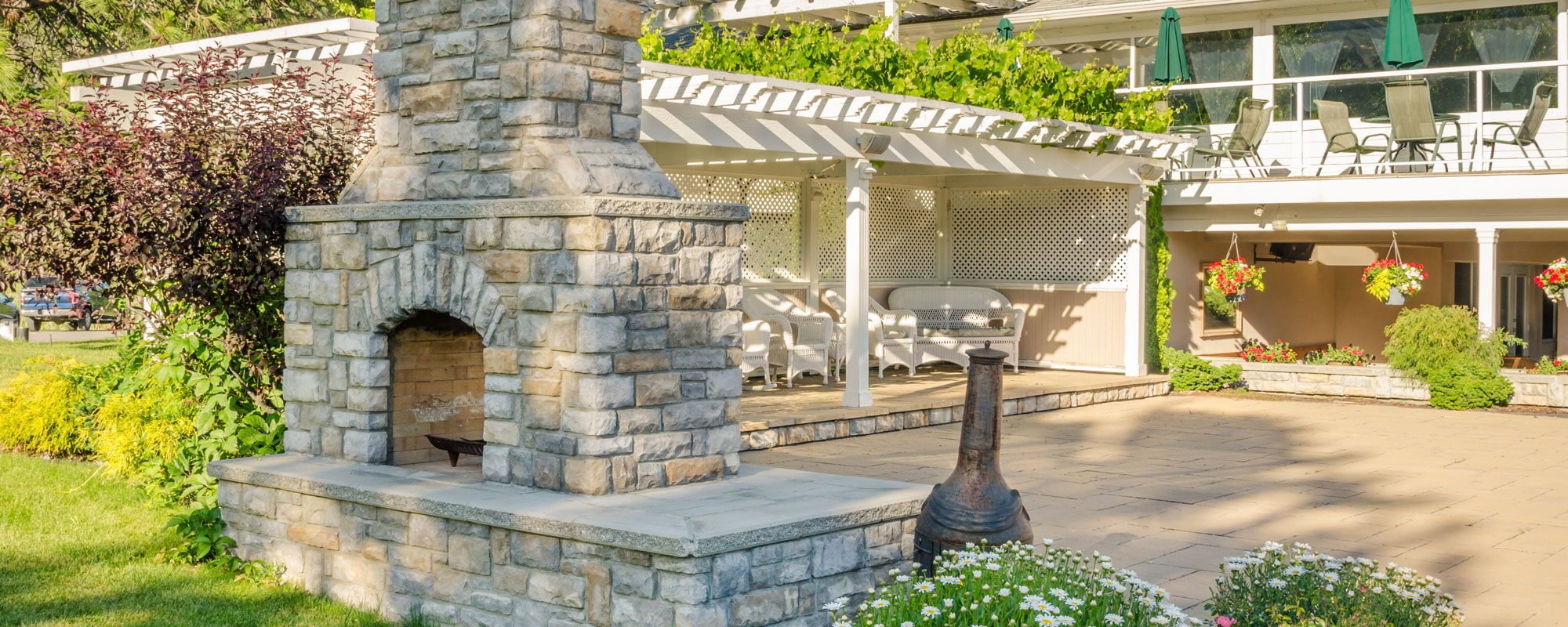 A stone outdoor fireplace and chimney on a patio beside a garden A stone outdoor fireplace and chimney on a patio beside a garden