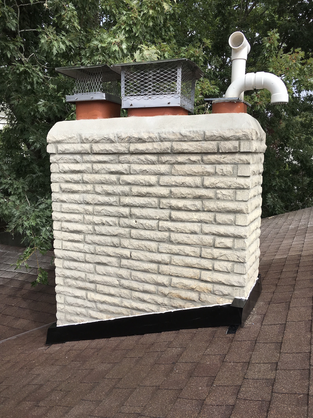 A painted brick chimney with a newly rebuilt crown and two flue caps A painted brick chimney with a newly rebuilt crown and two flue caps