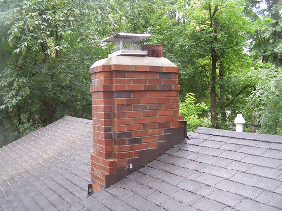 A red brick chimney on a shingle roof with new metal flashing at its base A red brick chimney on a shingle roof with new metal flashing at its base