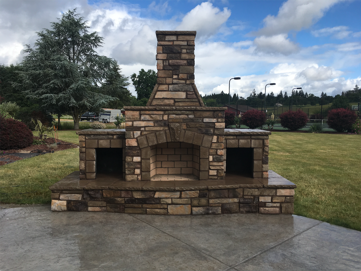 A stone outdoor fireplace with a tall chimney on a backyard patio A stone outdoor fireplace with a tall chimney on a backyard patio